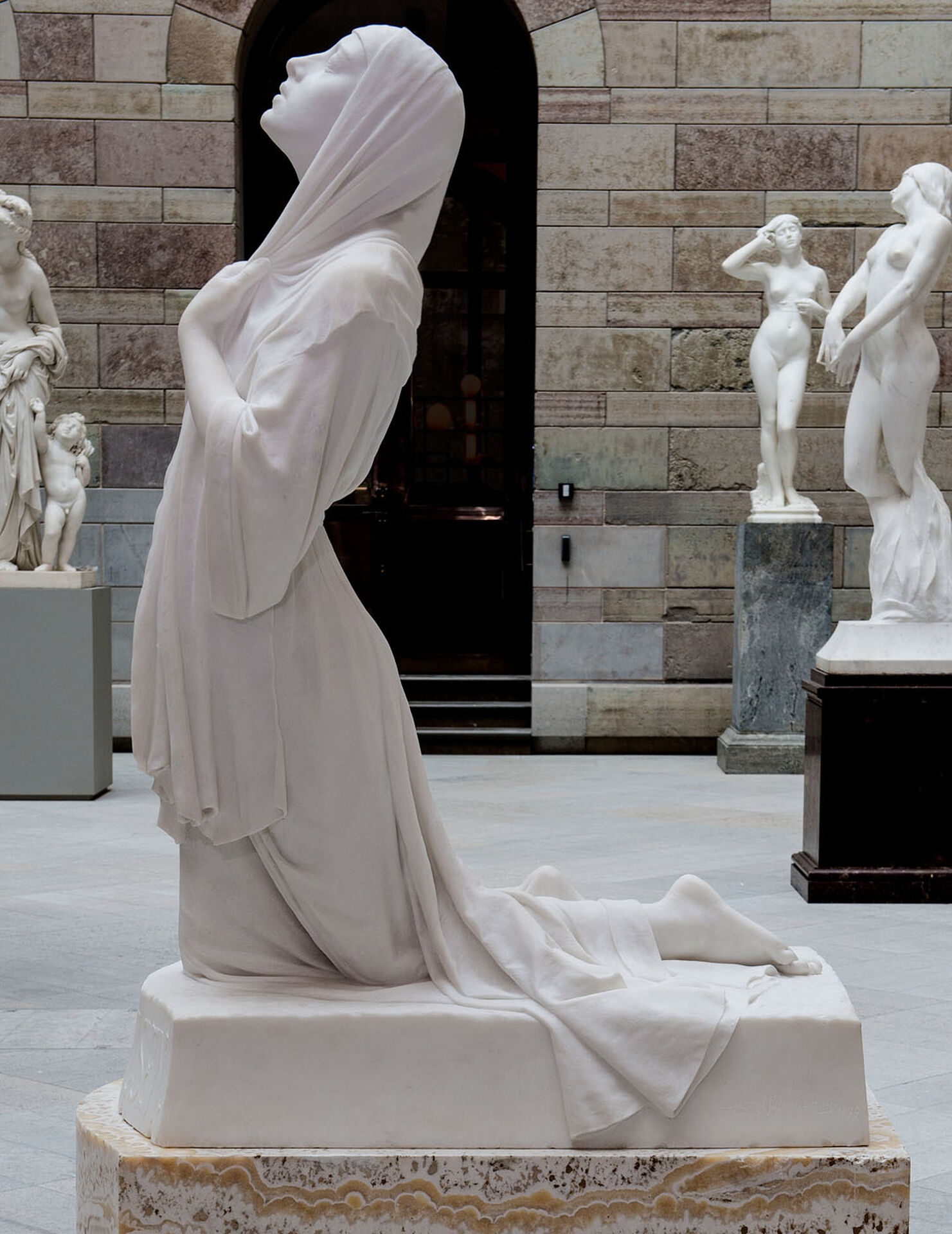 Marmorskulptur föreställande en knäböjande ung kvinna.