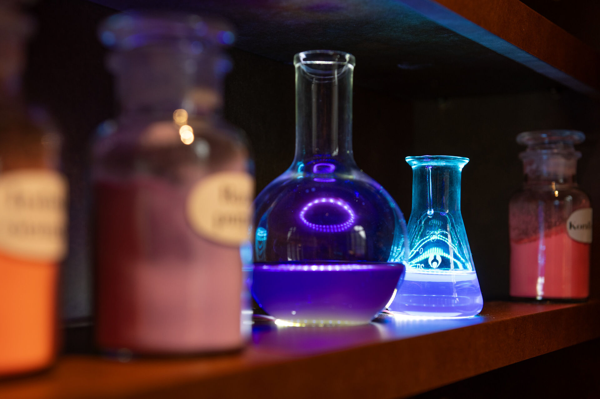 Laboratorieglas med färgade vätskor och flaskor med färgpigment som står på en hylla.