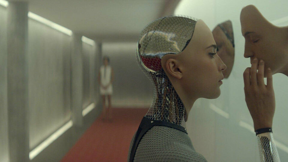Stillbild från filmen Ex Machina. Den kvinnliga roboten ser och tar på ett ansikte som stickcer ut från en vägg.