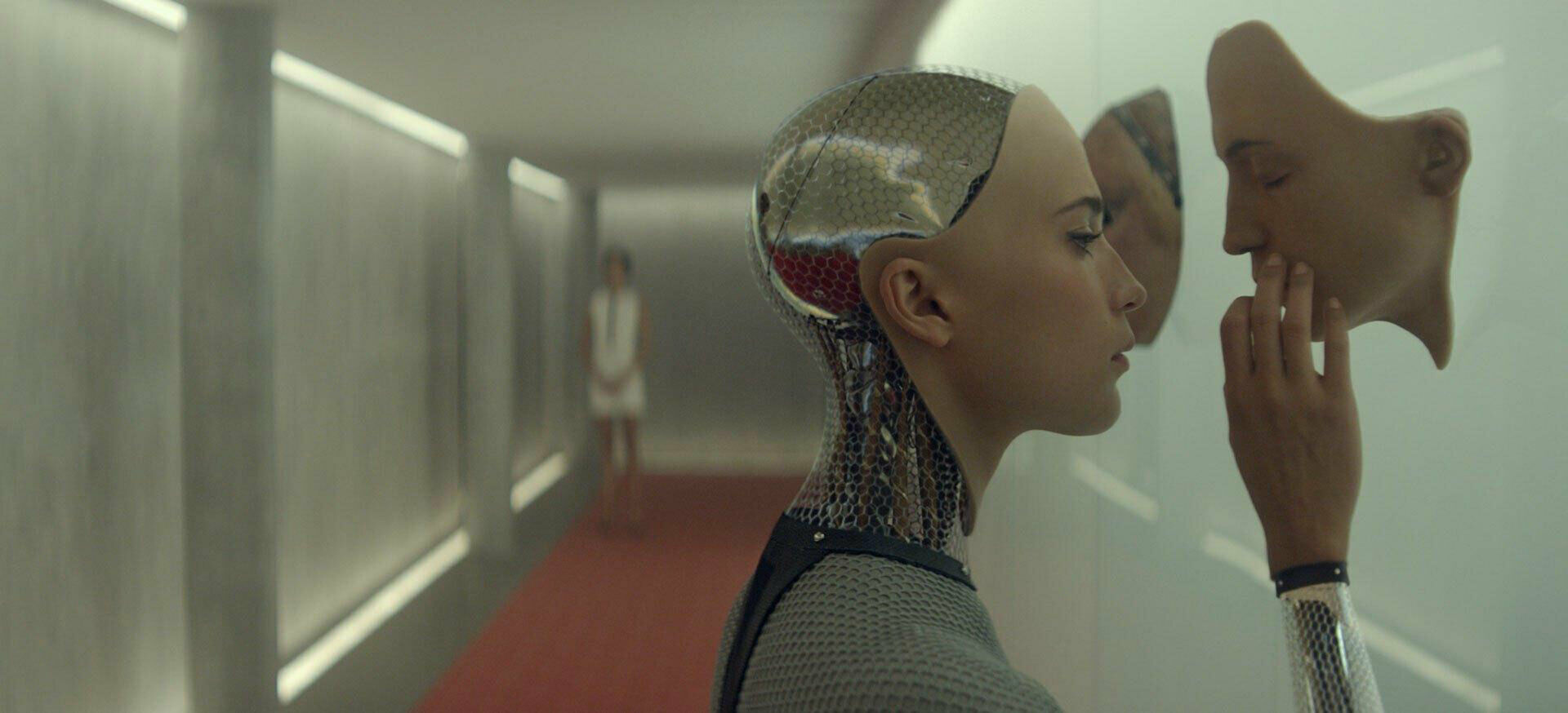 Stillbild från filmen Ex Machina. Den kvinnliga roboten ser och tar på ett ansikte som stickcer ut från en vägg.