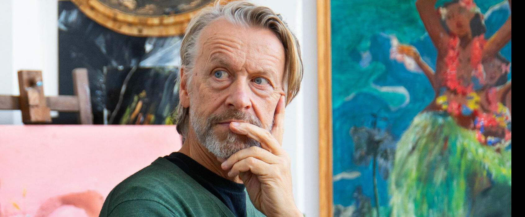 Fotografiskt porträtt av en man i en ateljé. Han vilar huvudet i ena handen och blickar snett bakåt. Han ser fundersam ut. I bakgrunden skymtar några tavlor.