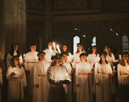 Kvinnor i luciatåg i miljö som ser ut att vara en kyrka.