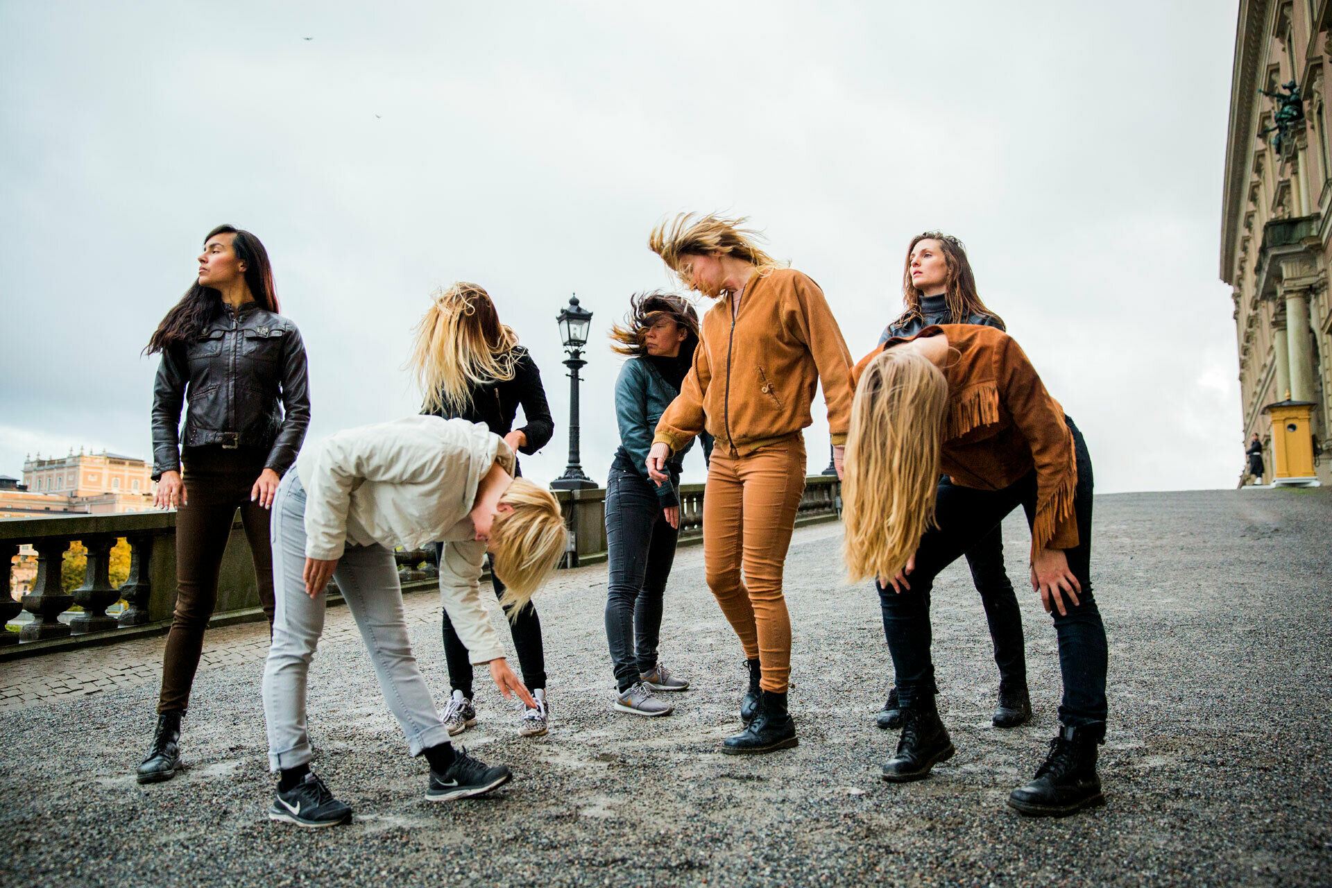 Några unga kvinnor som står i en klunga och nickar och skrapar med foten i marken, likt hästar.