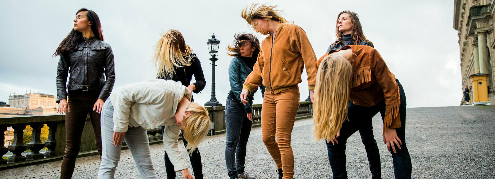 Några unga kvinnor som står i en klunga och nickar och skrapar med foten i marken, likt hästar.