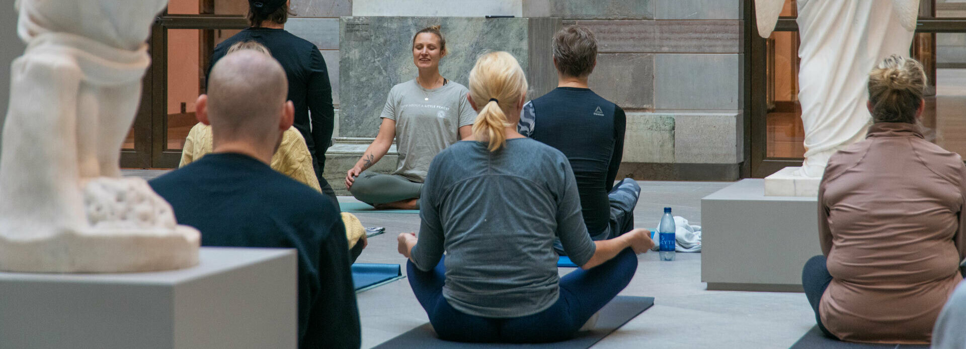 Några personer sitter och yogar bland skulpturer i en atriumgård.