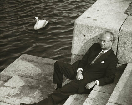 En man, Sveriges kung Carl XVI Gustav, som sitter i en trappa ner mot vattendrag.