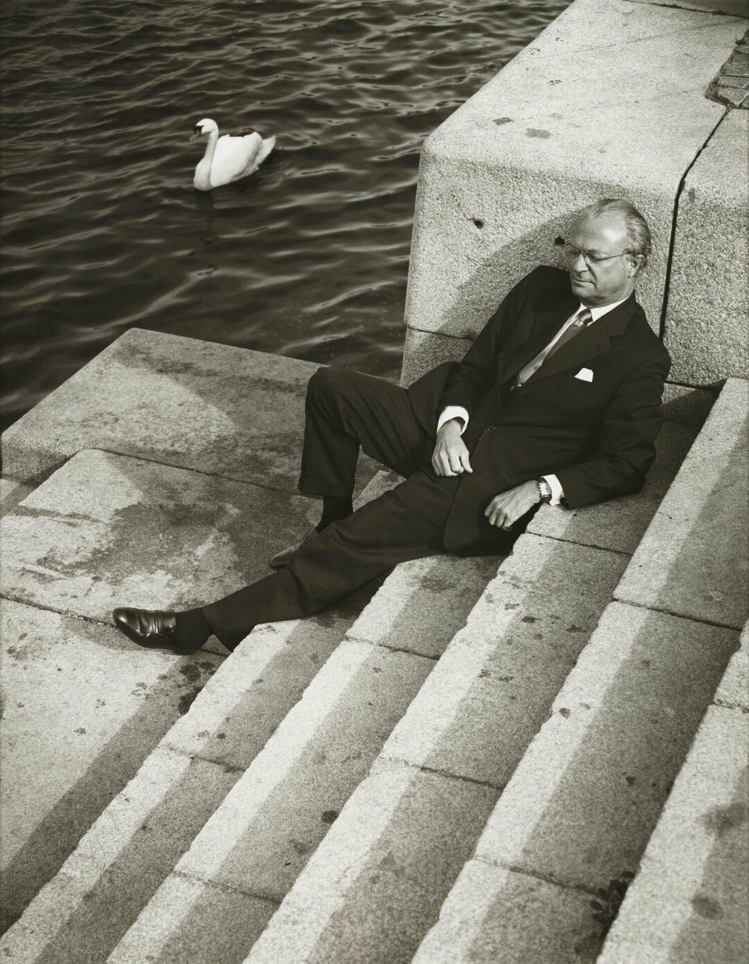 En man, Sveriges kung Carl XVI Gustav, som sitter i en trappa ner mot vattendrag.