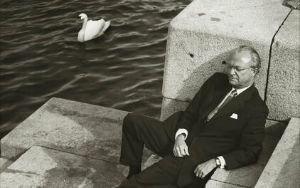 En man, Sveriges kung Carl XVI Gustav, som sitter i en trappa ner mot vattendrag.