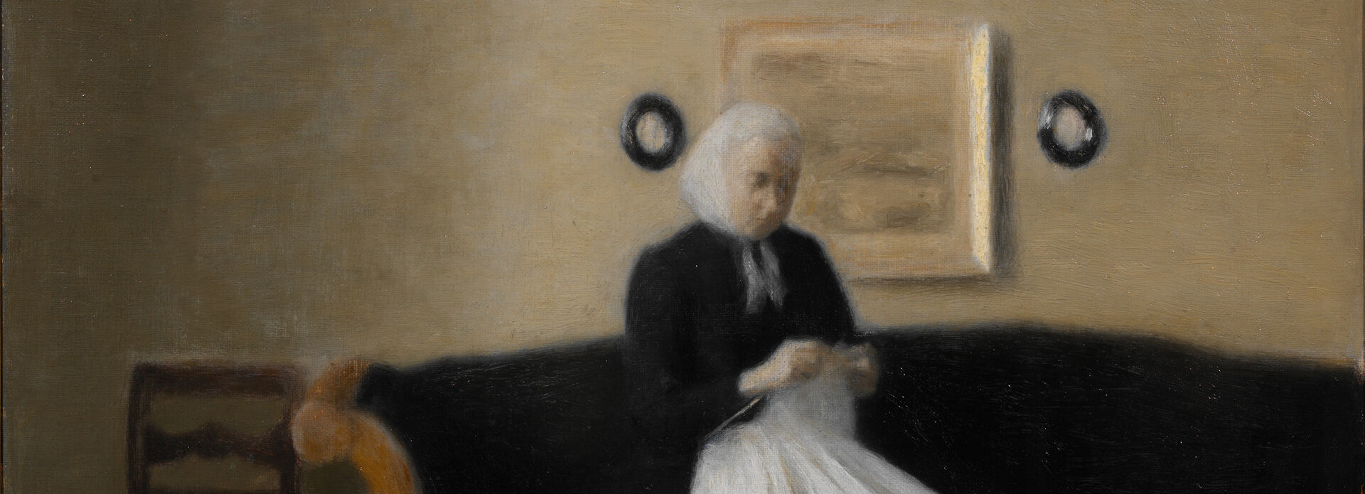 Äldre kvinna sittande i soffa med ett handarbete i händerna.