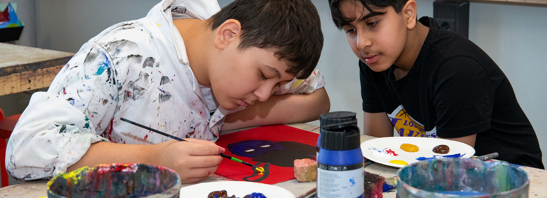 Två pojkar sitter och målar vid ett bord i en ateljé.