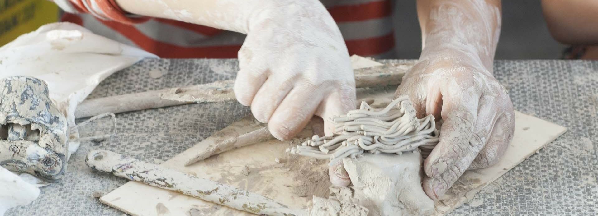 Armar och händer på ett barn som gör en figur i lera.