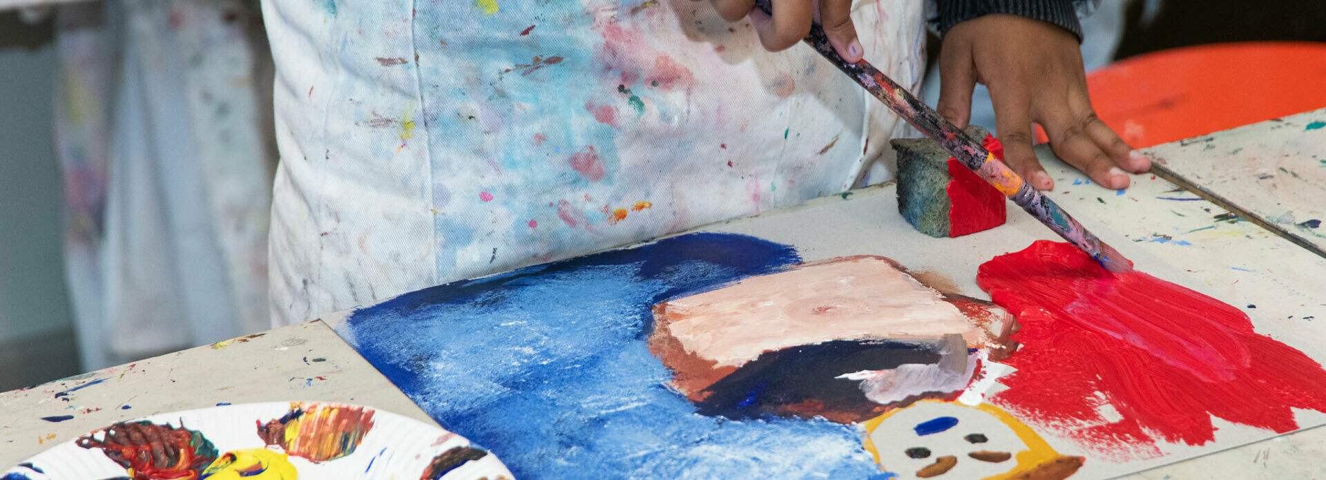 Händerna på ett barn som målar ett porträtt med akrylfärg.