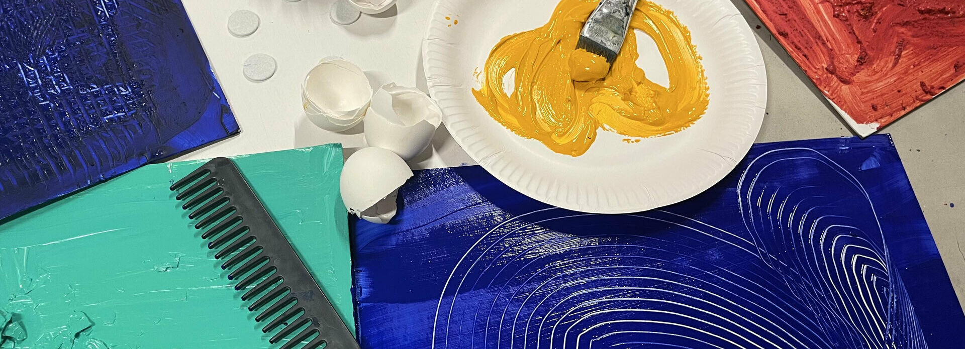 Äggskal, en pensel och färg på en tallrik, bemålade papper samt en kam.