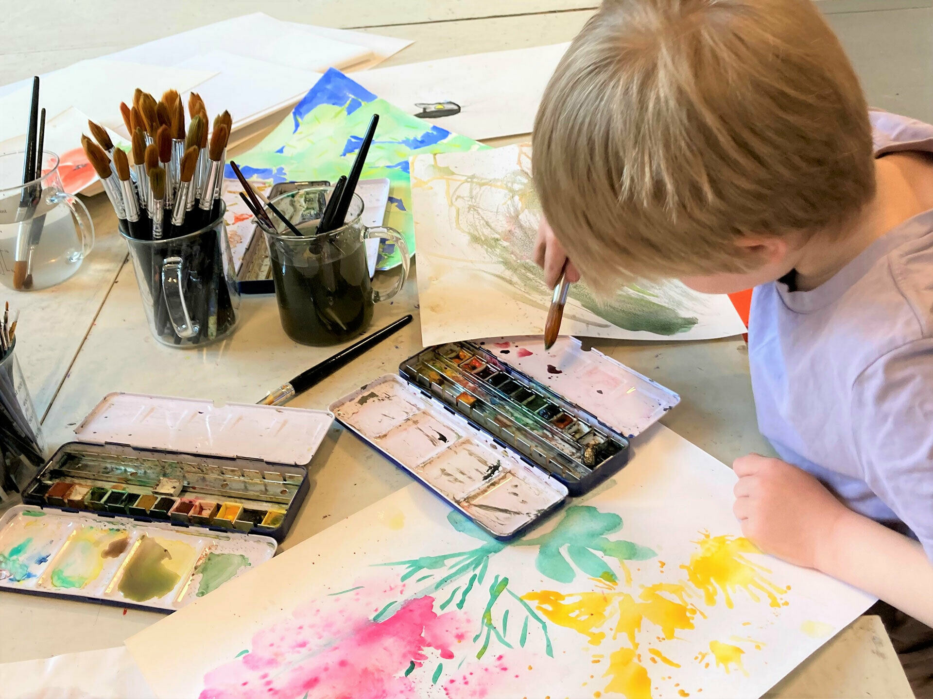 En pojke som sitter vid ett bord och målar med akvarellfärg.