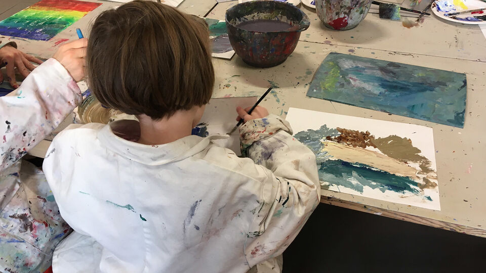 Barn som sitter vid bord i en ateljé och målar med vattenfärg.