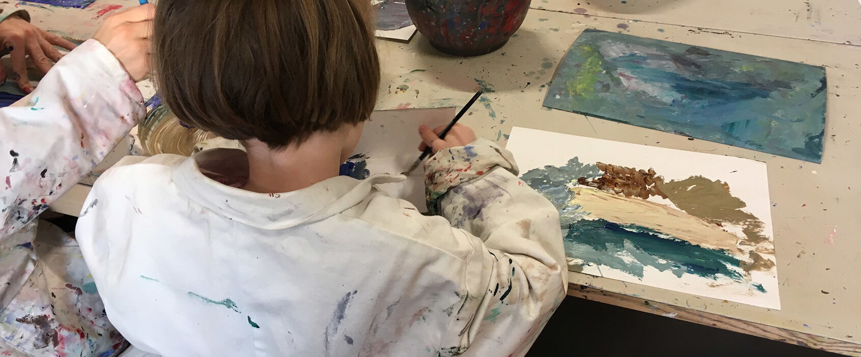 Barn som sitter vid bord i en ateljé och målar med vattenfärg.