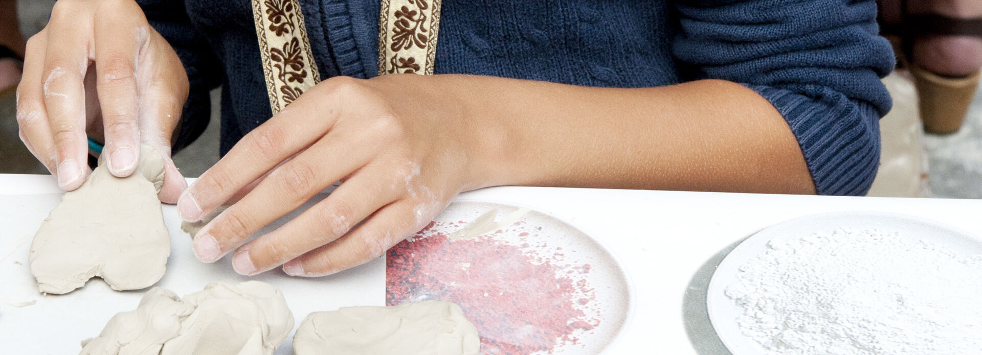 Händerna på ett barn som sitter vid ett bord och formar ett hjärta i lera.