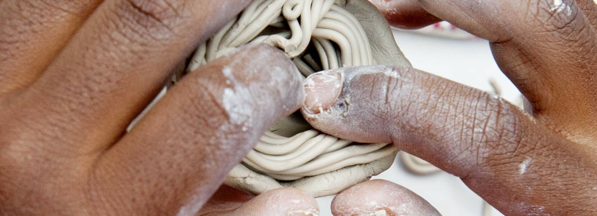 Händerna på ett barn som tillverkar en figur i lera.