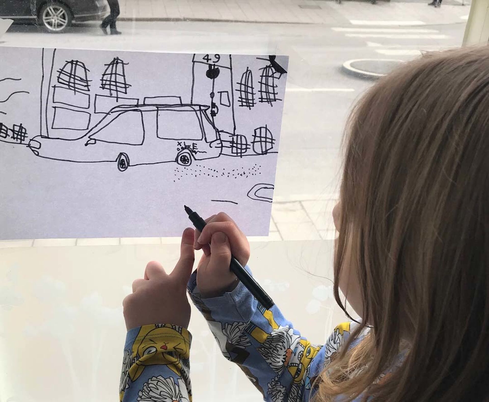 Ett barn står vid ett fönster och ritar av utsikten.