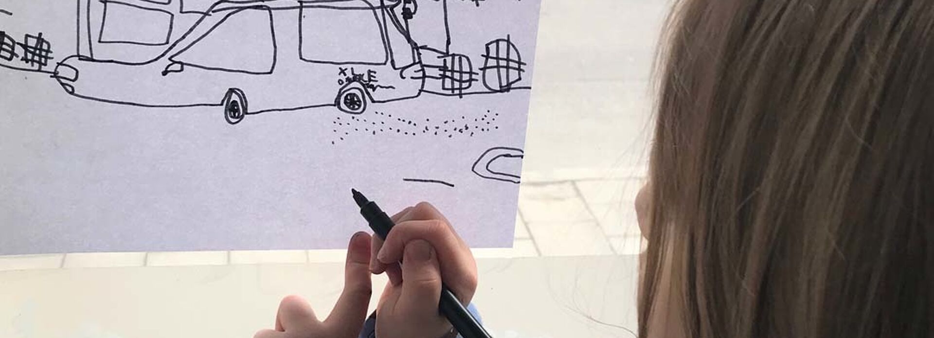 Ett barn står vid ett fönster och ritar av utsikten.