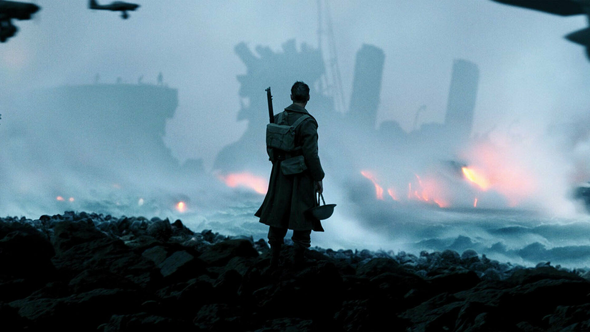 En soldat står med ryggen mot betraktaren. Han tittar ut över ett skummande hav där konturerna av ett fartyg i brand syns genom krutrök och mörker.