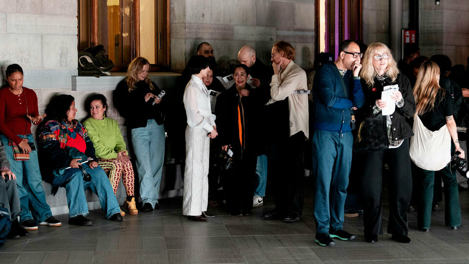 Människor som står och sitter, några talar med varandra, i en stor museihall.