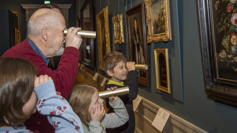 En äldre man och tre barn tittar på tavlor i en museisal med hjälp av hemmagjorda kikare, eller tittinstrument.