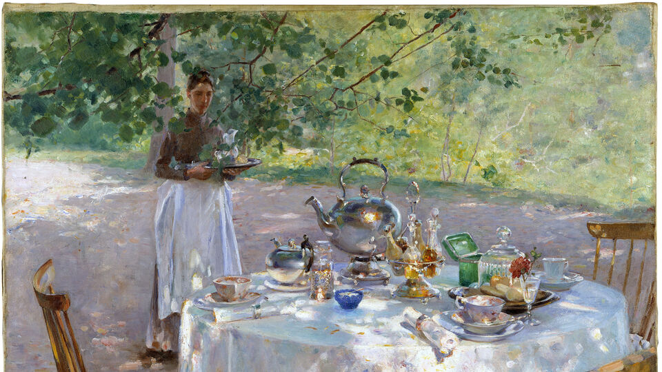穆尔宁av ett uppdukat bord med tekittel，koppar och glas utomhus。En kvinna med vitt förkläde bär páEn bricka。