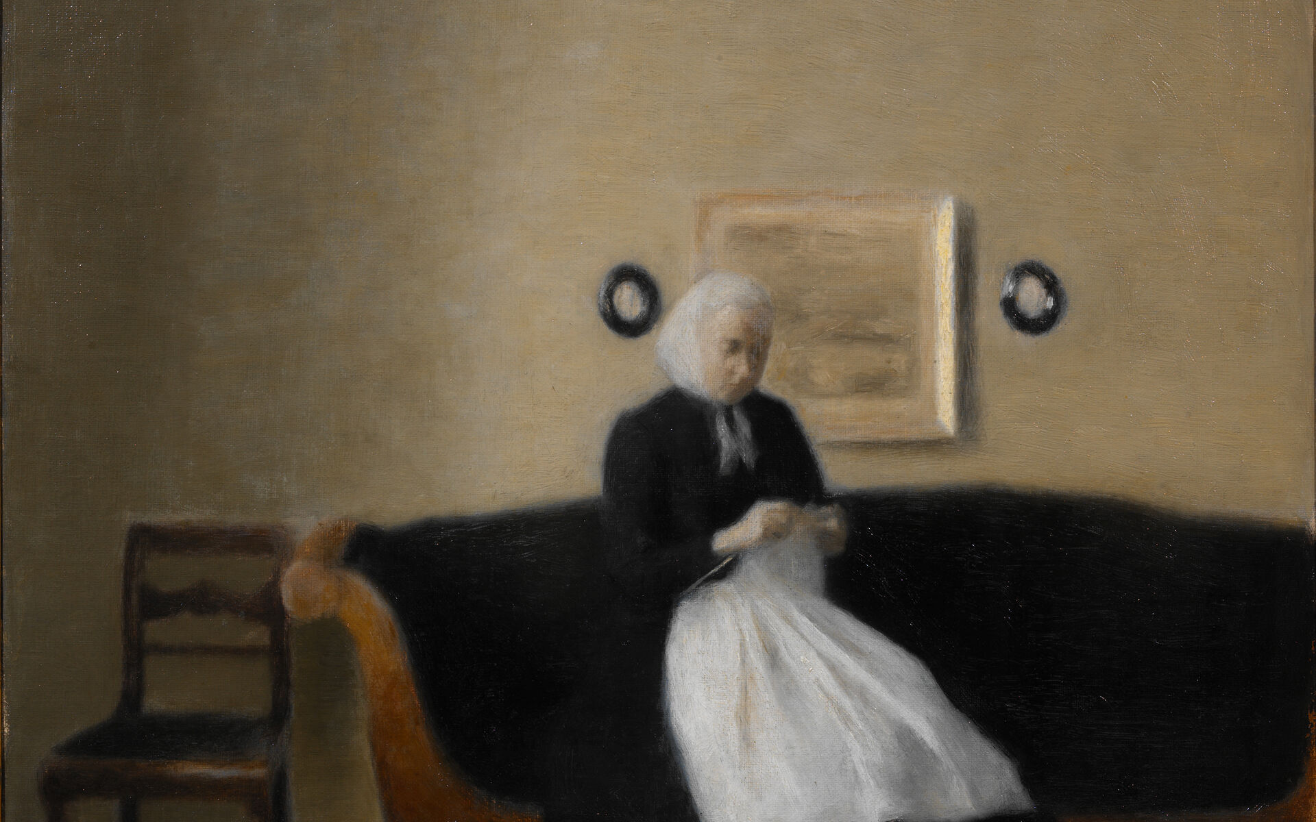 Äldre kvinna sittande i soffa med ett handarbete i händerna.
