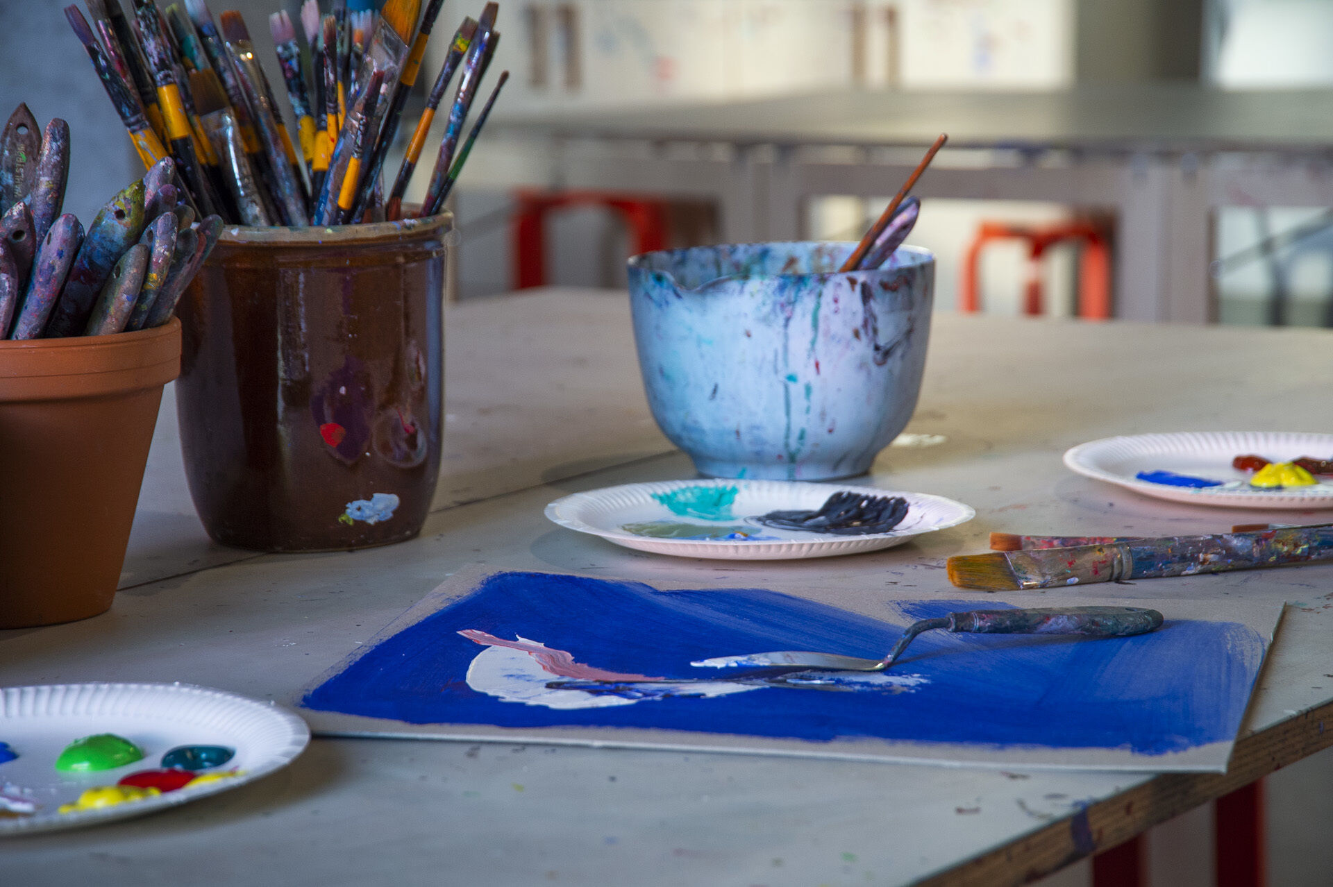 Bunkar med penslar, tallrikar med färg och papper med målat alster i en ateljé.