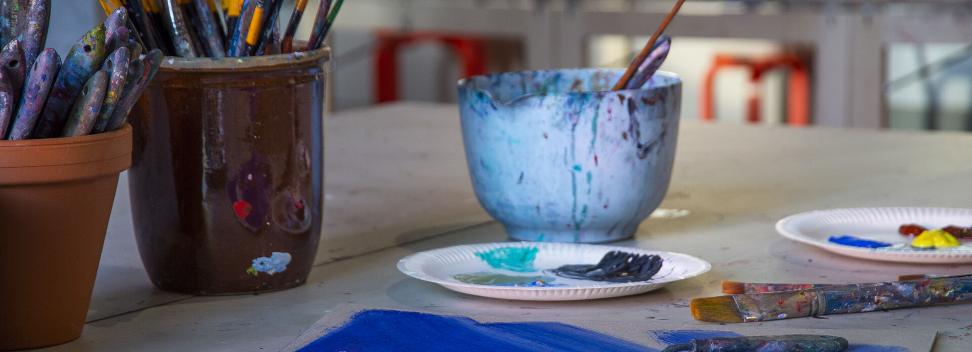 Bunkar med penslar, tallrikar med färg och papper med målat alster i en ateljé.