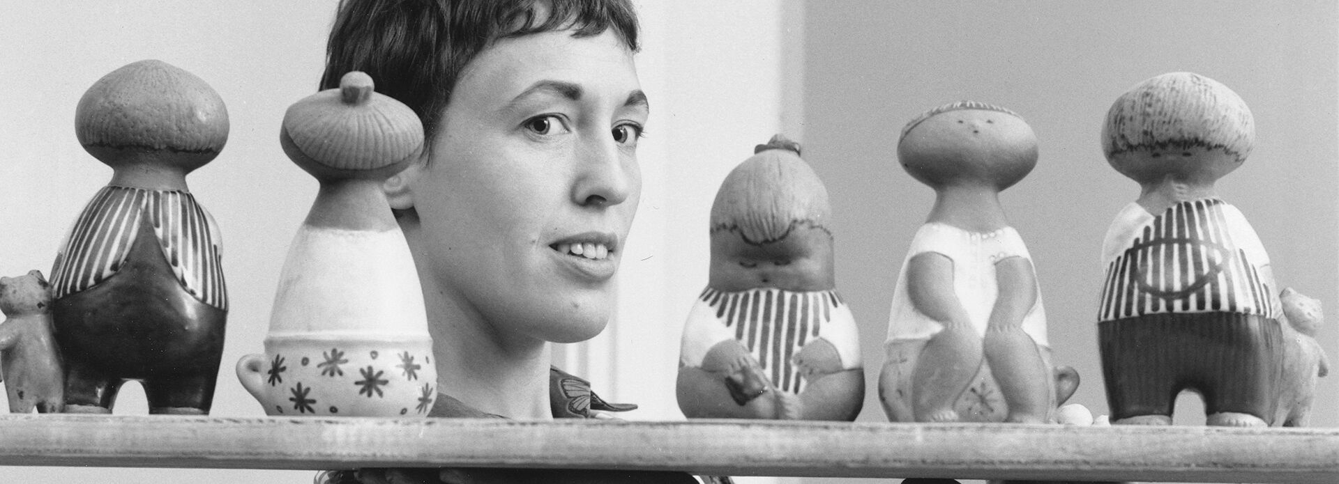 kvinna håller upp hylla med keramikfigurer.