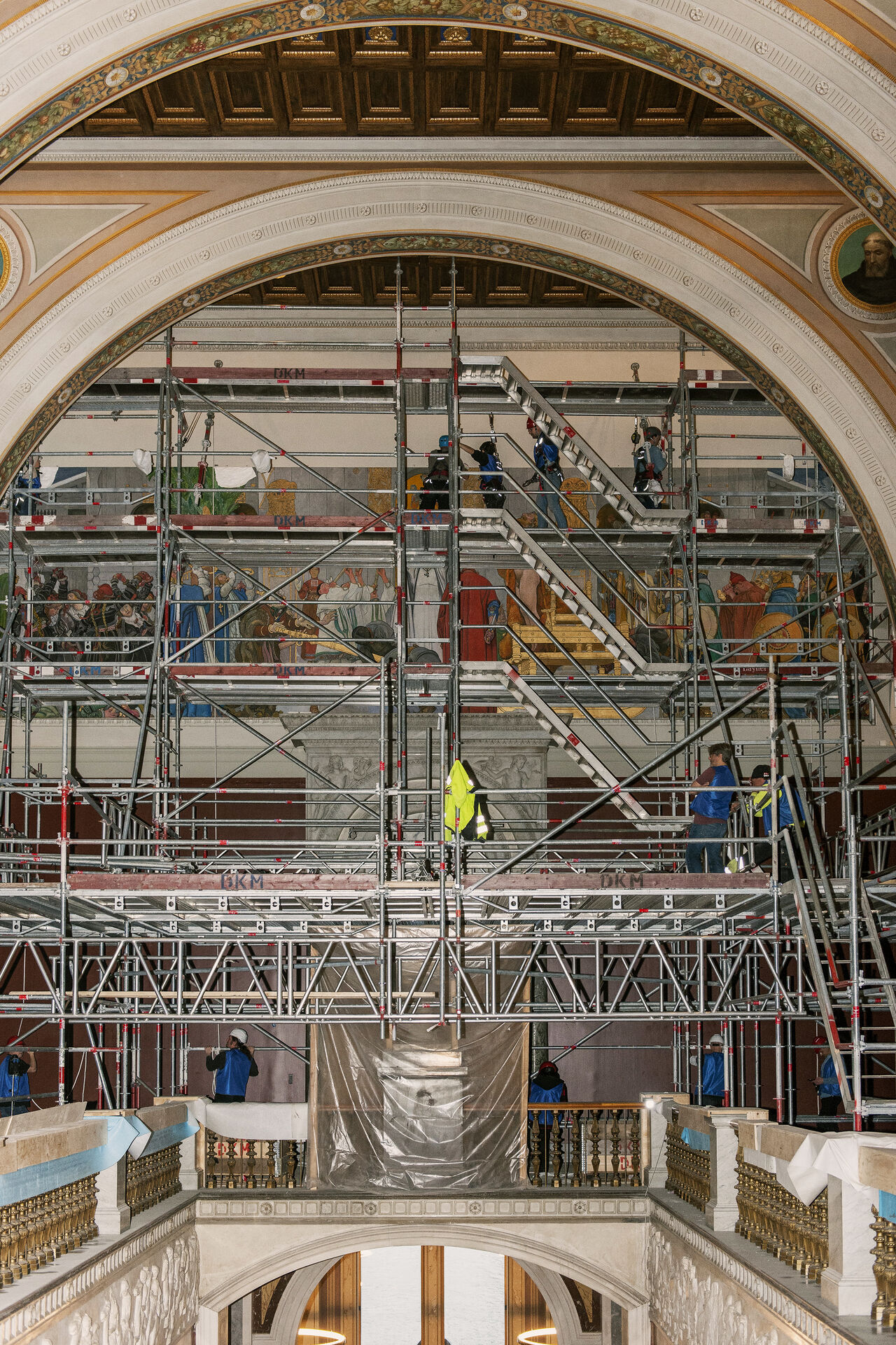 Personal på byggställning framför målningen Midvinterblot som håller på att fästas på plats.