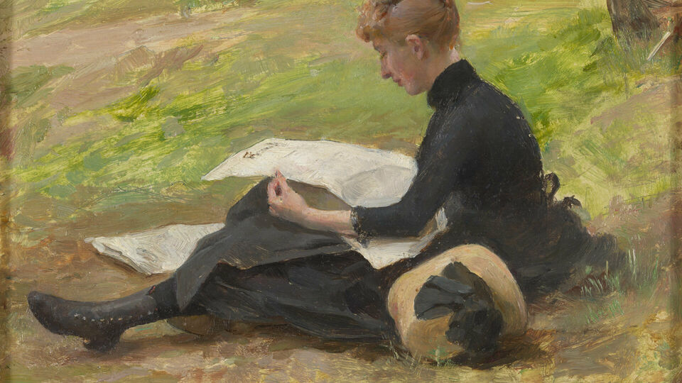 En kvinna i svart klänning som sitter på gräset och läser en tidning.