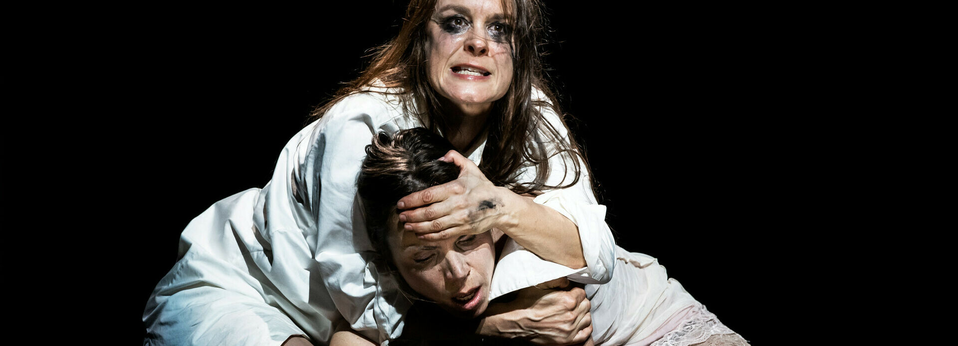 Två skådespelare i en stark och känslosam scen. De ligger på huk och den ena håller fast den andra i huvudet.