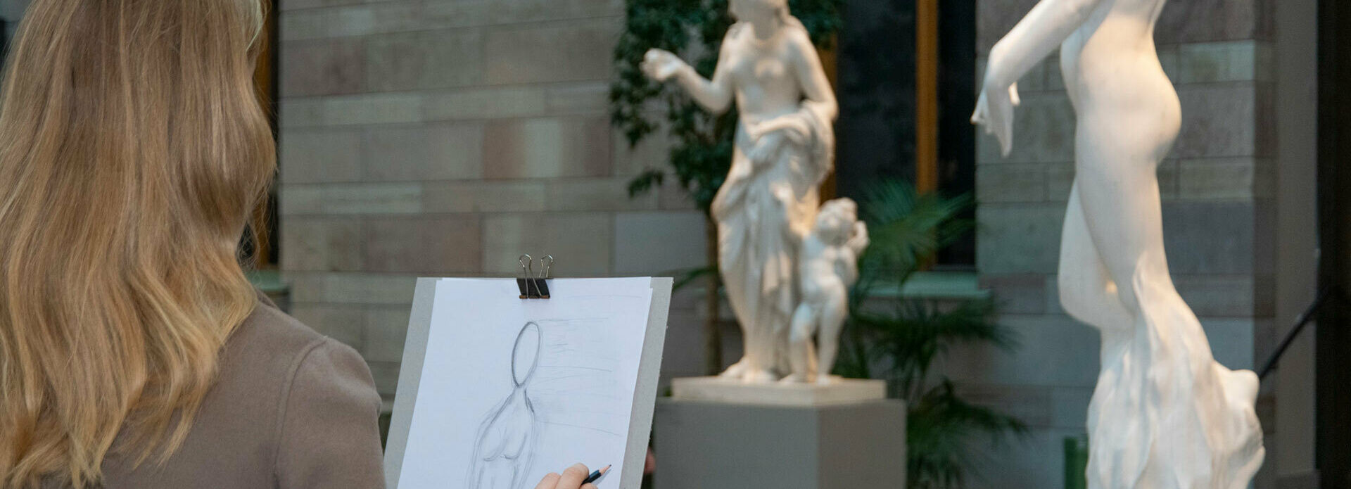 En person står i en atriumgård och tecknar av vita marmorskulpturer.