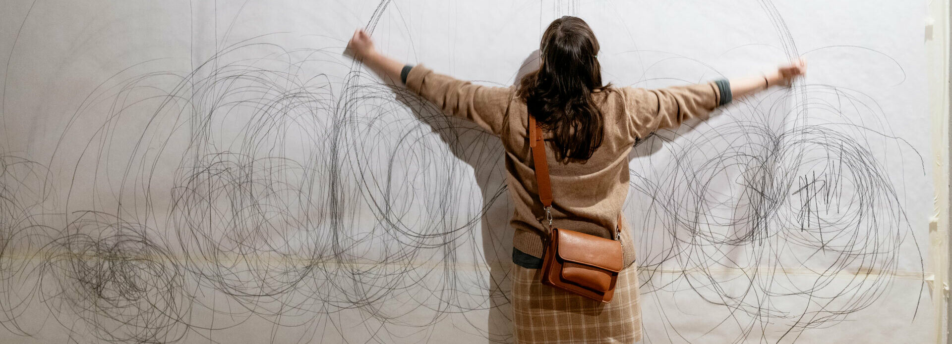 En kvinna som står med ryggen mot betraktaren. Hon håller ut bägge armarna och ritar på ett stort papper uppspänt på en vägg.