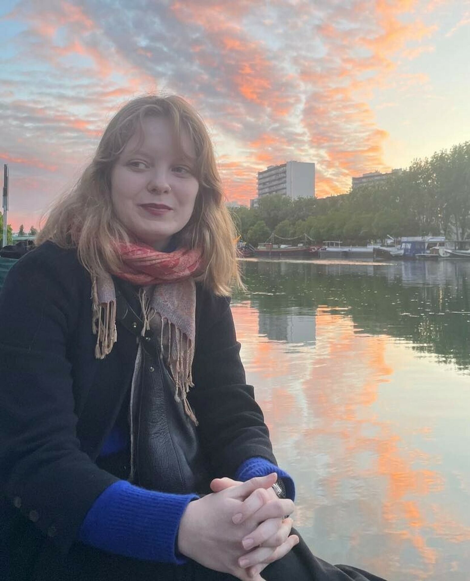 Porträttfoto av en ung kvinna framför en flod med bakomliggande grönska och bebyggelse.