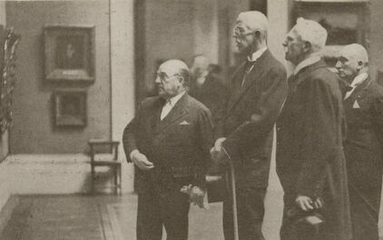 Äldre fotografi föreställande några män, bland andra kung Gustav V, som tittar på målningar som hänger på en museivägg.