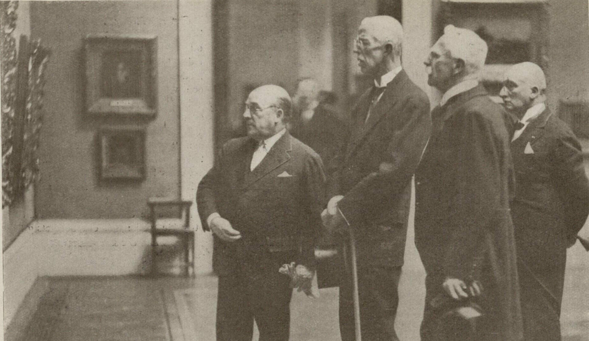 Äldre fotografi föreställande några män, bland andra kung Gustav V, som tittar på målningar som hänger på en museivägg.