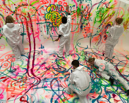 Några personer som målar gemensamt på ett stort kollektivt konstverk.