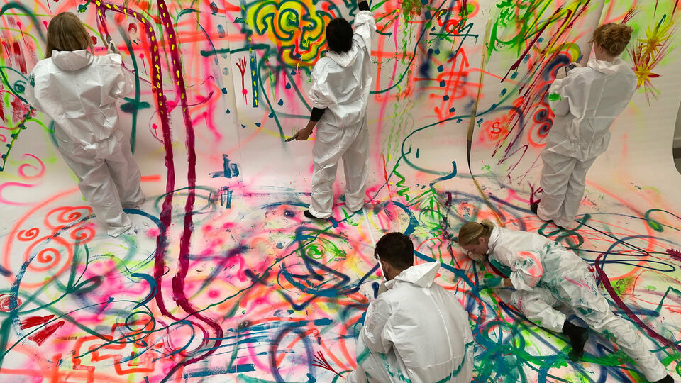 Några personer som målar gemensamt på ett stort kollektivt konstverk.