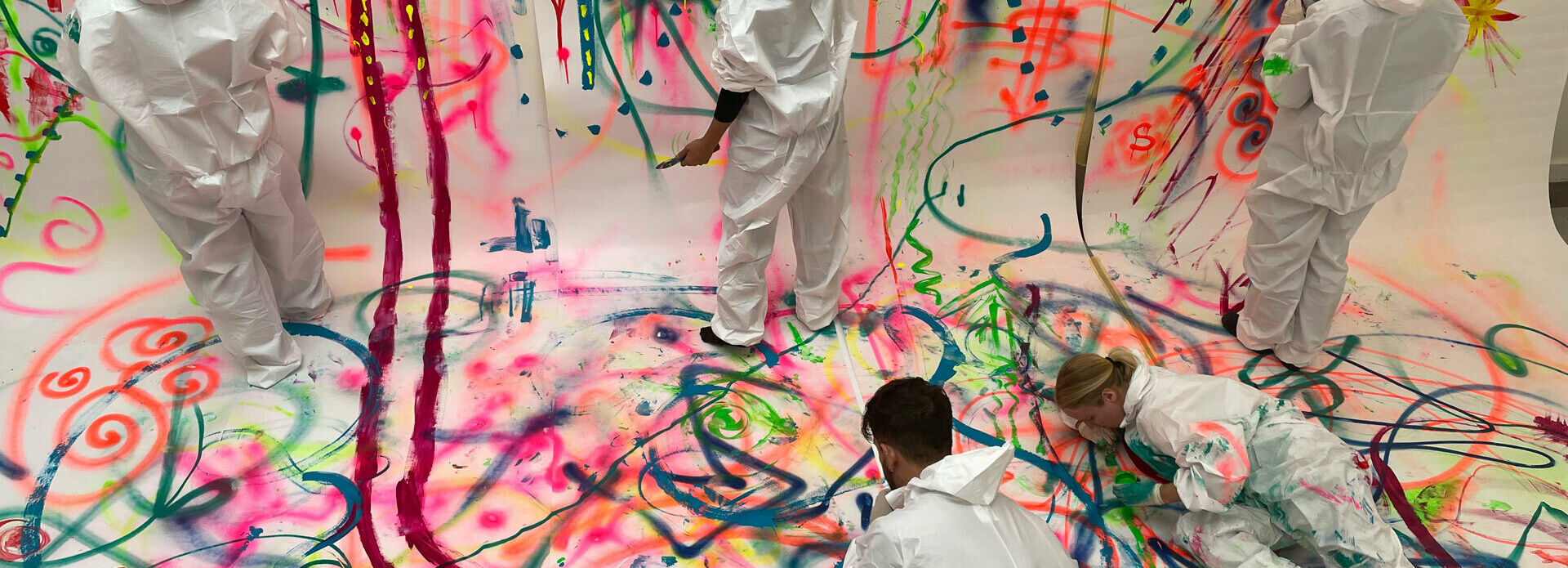 Några personer som målar gemensamt på ett stort kollektivt konstverk.