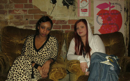 Två unga kvinnor som sitter i varsin fåtölj i ett rum som ser ut som en replokal eller liknande.