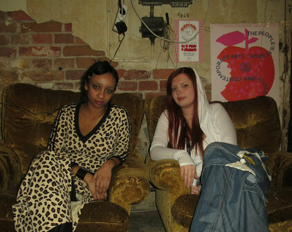 Två unga kvinnor som sitter i varsin fåtölj i ett rum som ser ut som en replokal eller liknande.