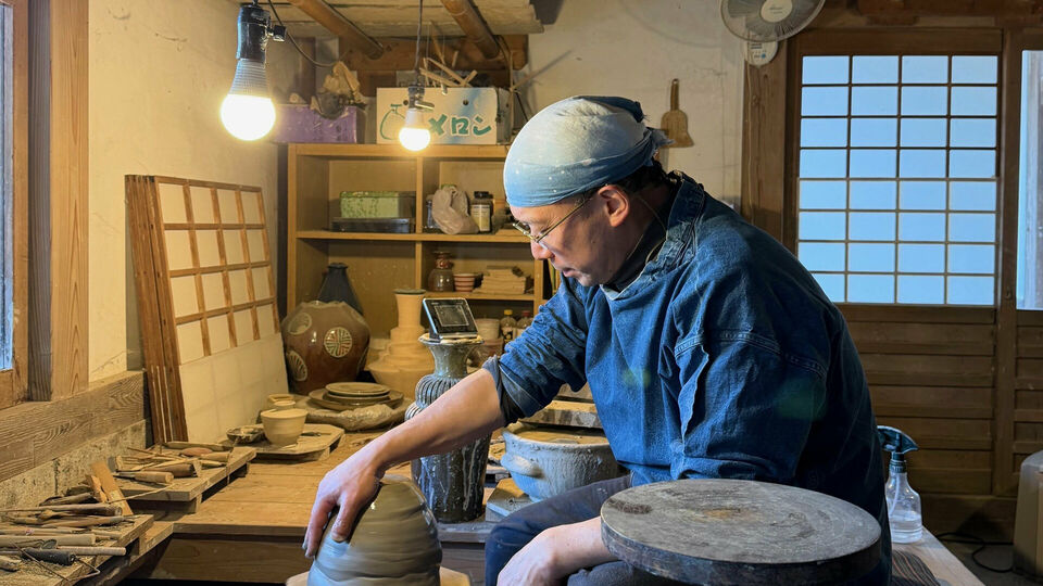 En man som sitter på huk och drejar i en keramikverkstad.
