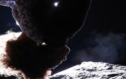 En person som tycks hänga upp och ner, med månlandskap bakom sig.