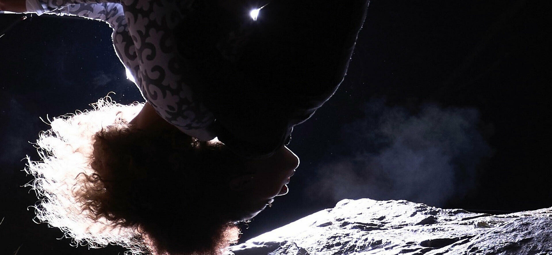 En person som tycks hänga upp och ner, med månlandskap bakom sig.