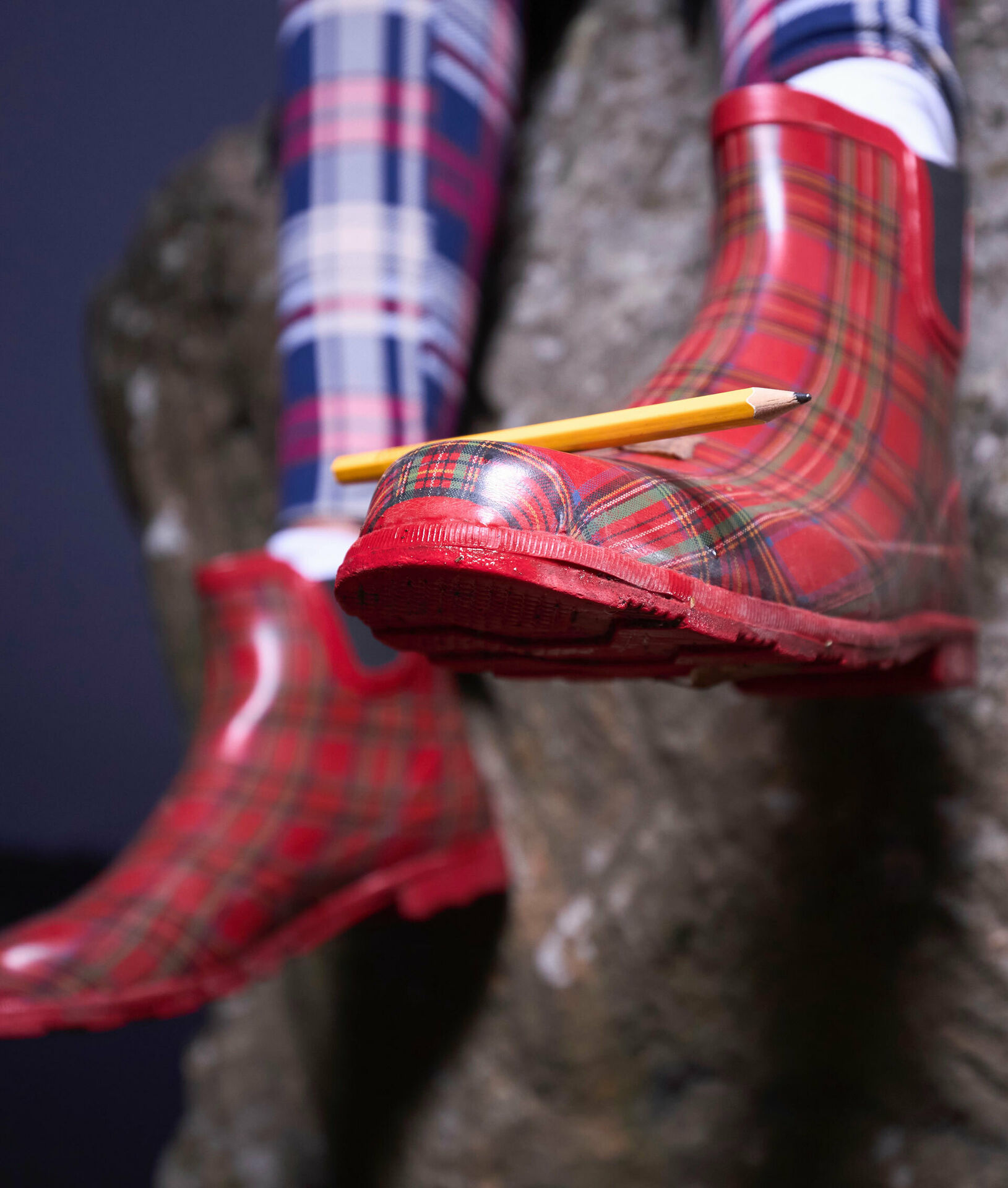 Ben och fötter iklädda rutiga trikåer och gummistövlar. På ena foten balanserar en bkyertspenna.