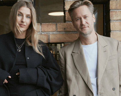 Fotografiskt dubbelporträtt av en kvinna och en man som står framför en tegelvägg.